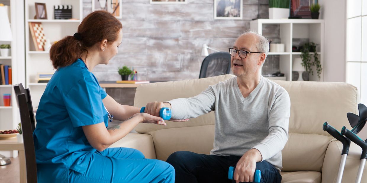 Senior man in nursing home with dumbbells doing physiotherapy with help from nurse.