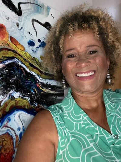 Smiling woman with curly hair stands in front of colorful abstract art.