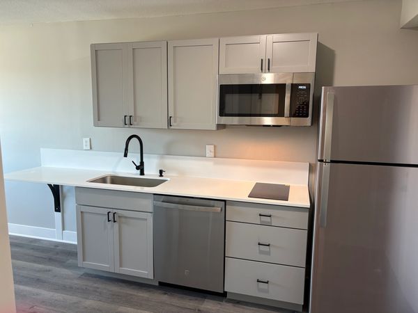 Modern kitchen with gray cabinets, stainless steel appliances, and white countertops.