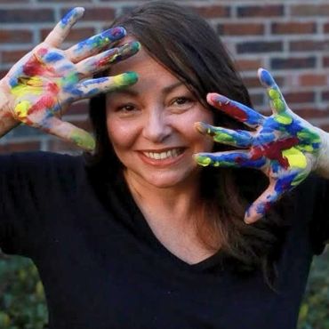woman standing in front of a brick wall with paint on her hands