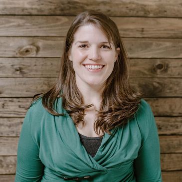 female counselor smiling 
and standing in front of a wood wall