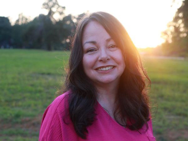 female counselor smiling standing in a field with the sun behind her 