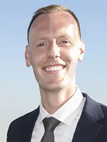 A smiling man in a suit with a clear blue sky background.