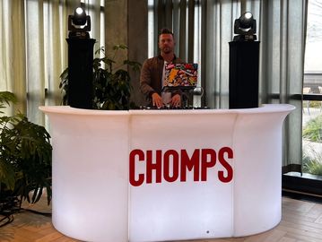 Man DJing behind illuminated CHOMPS bar.
