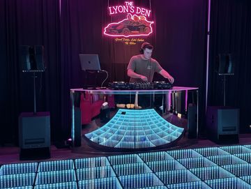 DJ performing at The Lyon's Den with illuminated dance floor.