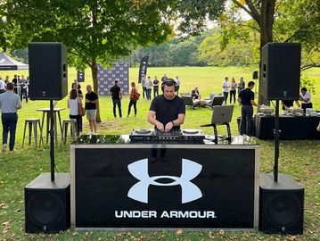 DJ performing behind Under Armour booth outdoors.