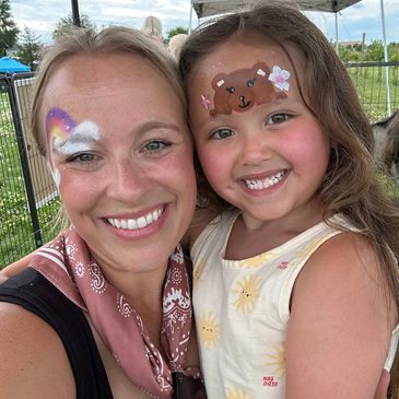 Smiling woman and child with face paint at outdoor event.