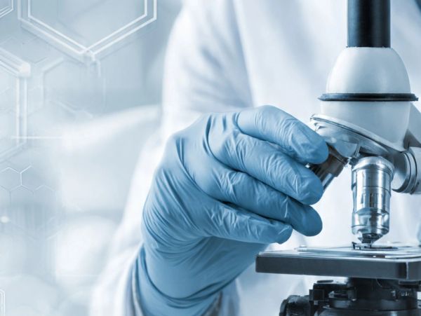 Scientist adjusting microscope with gloved hand in a lab.