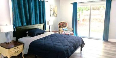 Bright bedroom with navy blue bedding and teal curtains overlooking a garden.