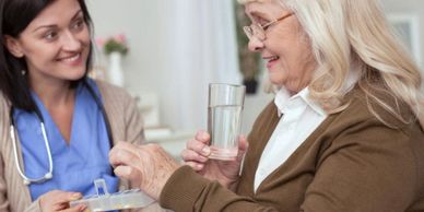 A nurse helps an elderly woman take her medication with water.