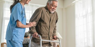Nurse assisting elderly man with walker in bright room.