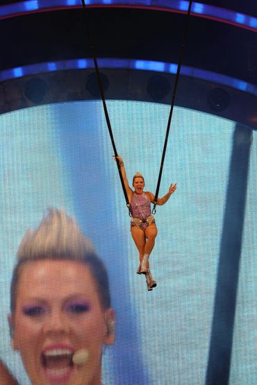 Female singer Pink swings high in the air above a stage. 