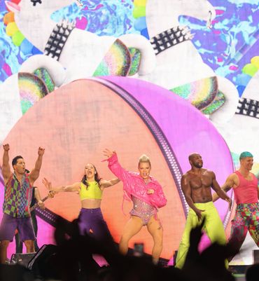 Pink and backup dancers stand in front of a giant projection of a beach ball. 