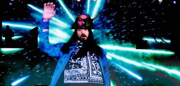 DJ and electronic music producer Steve Aoki plays on a stage with a giant image of himself. 
