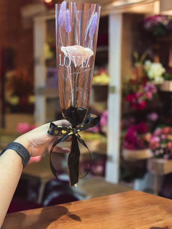 Hand holding a single wrapped white rose with "LOVE." printed on the wrapping.