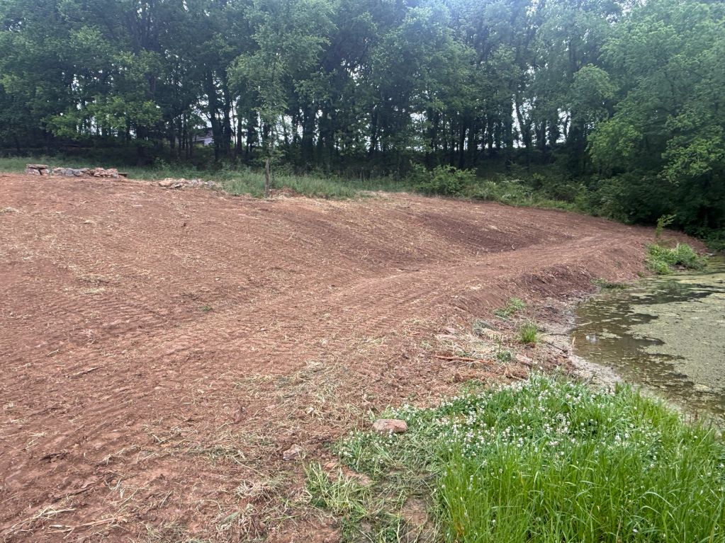 Freshly plowed land next to a pond with trees in the background.