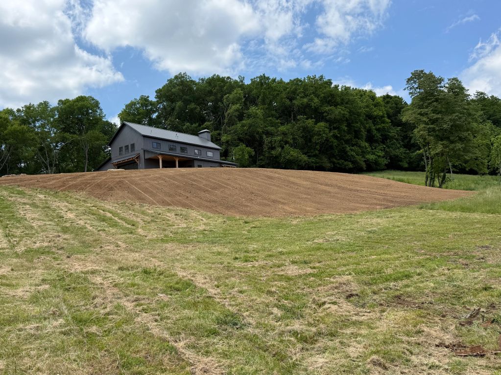 Modern house near a freshly plowed field with trees in the background.
