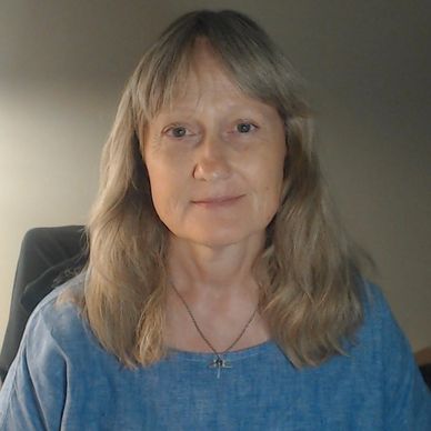 A woman with blonde hair smiling softly, wearing a blue top.