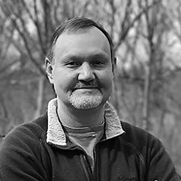 Smiling man with crossed arms outdoors in a black and white photo.
