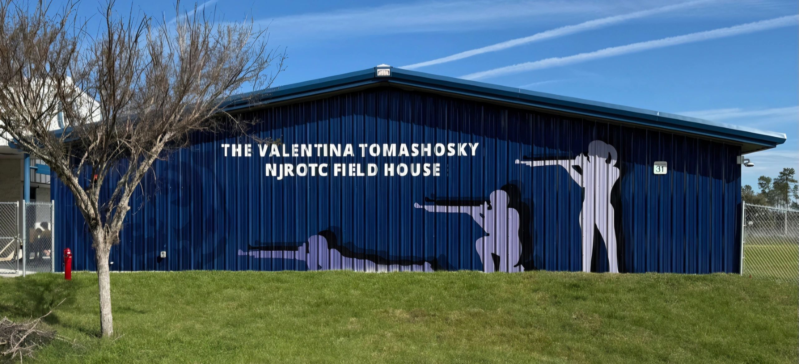 Mural on a blue building shows three shooters with rifles and text about NJROTC Field House.