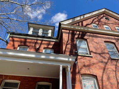 Brick building with white columns under a blue sky and tree shadows.