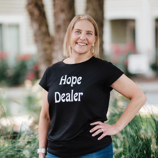 Smiling woman wearing a "Hope Dealer" t-shirt outdoors.
