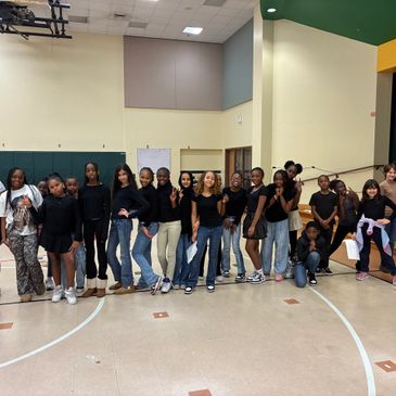 A diverse group of young people posing indoors, mostly dressed in black.