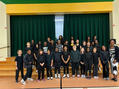A diverse group of children and a teacher posing on a stage in a school auditorium.