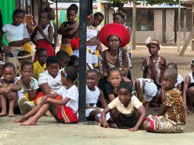 Group of children and adults gathered outdoors, some in traditional attire.
