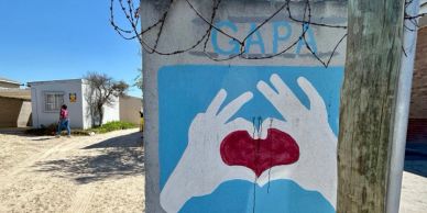 Street art of hands forming a heart shape with a red heart inside, painted on a blue background.