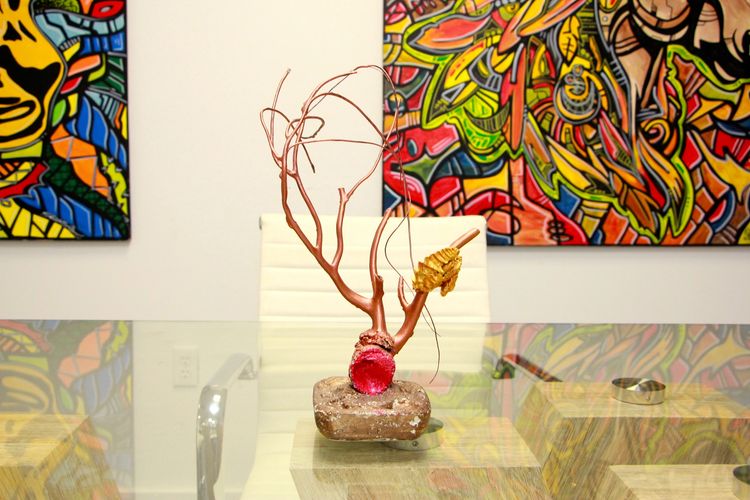Glass table with driftwood painted sculpture. Two abstract art pieces on the wall behind the table.