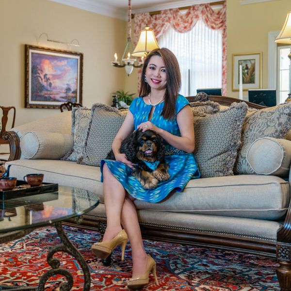 Woman in blue dress sitting on a couch with a small dog in a cozy living room.