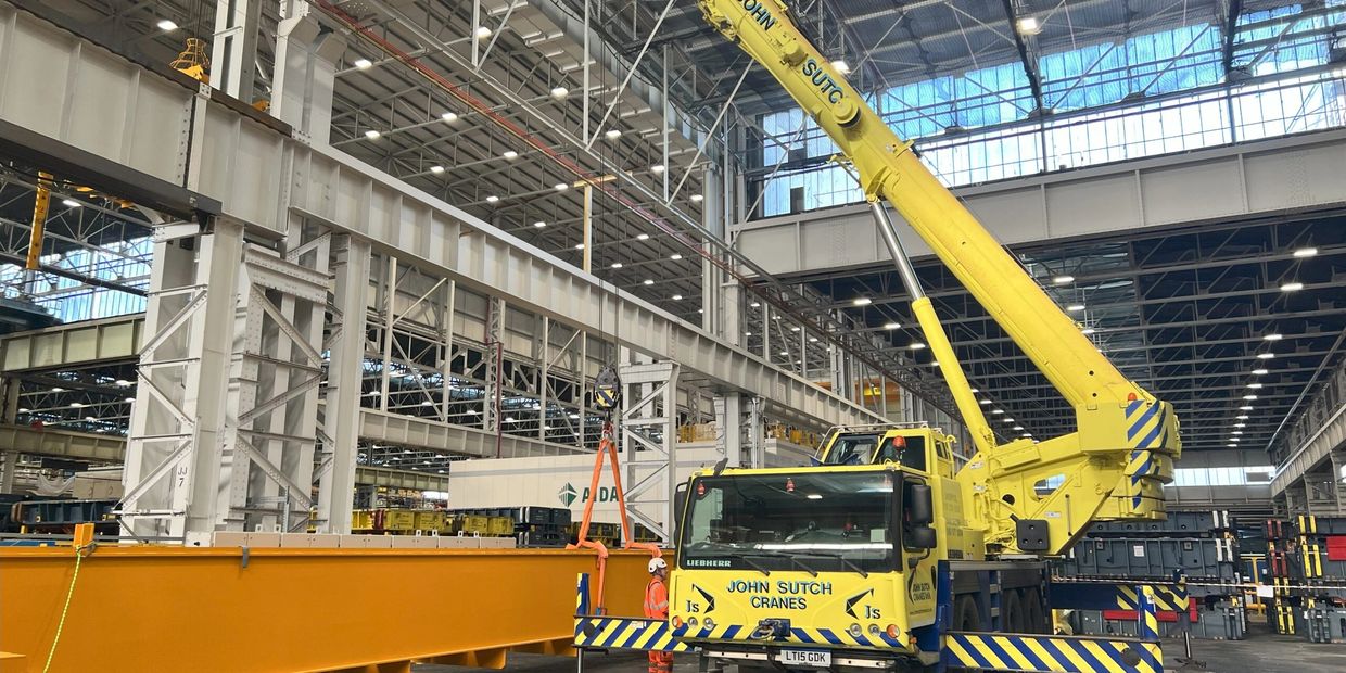Large yellow crane lifting a beam inside an industrial warehouse.