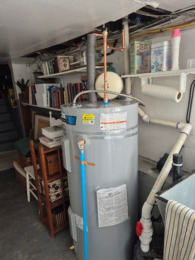 A gray water heater with pipes in a basement storage area.