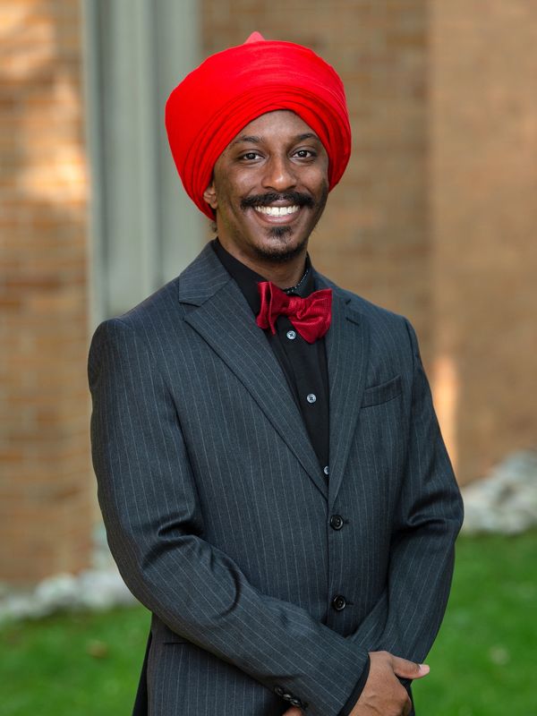 Man in a red turban and bow tie with a pinstripe suit.