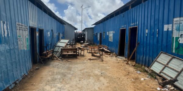 Unpaved pathway between blue container-like structures with scattered furniture.