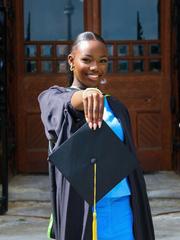 Smiling graduate holding a cap towards the camera.