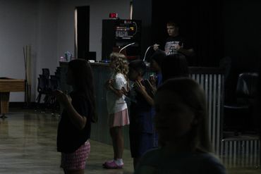 Children standing in a dimly lit room, some with hands raised.