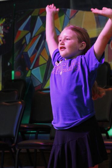 A young girl raising her arms joyfully indoors with colorful geometric wall art.