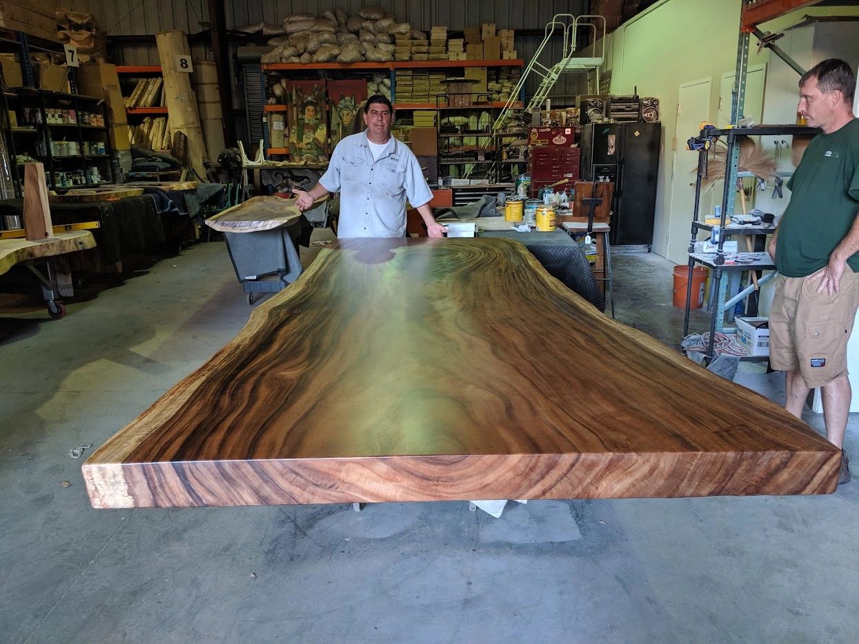 Craftsmen stand by massive live-edge slab being made into a dining table in fabrication warehouse