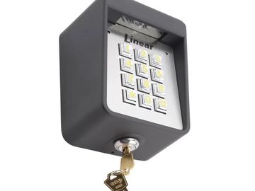A black keypad lock box with a silver face and a key inserted.