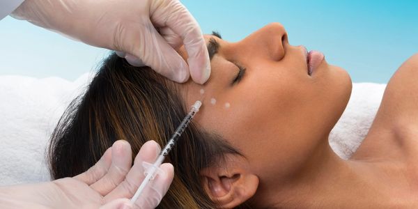 A women getting a shot in the right side of her face by a medical person with gloves.