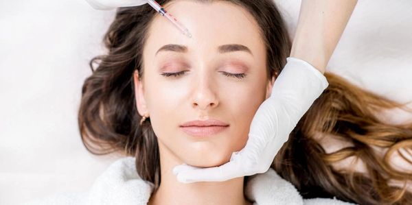 Brunette women in a spa getting a Botox shot in her forehead by a medical person.