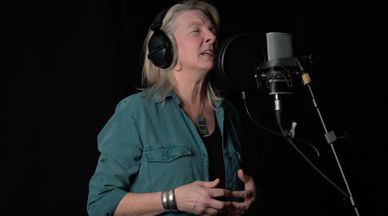 Woman singing passionately into a studio microphone with headphones on.