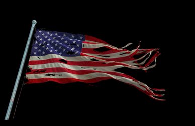 A torn and tattered American flag waving against a black background.