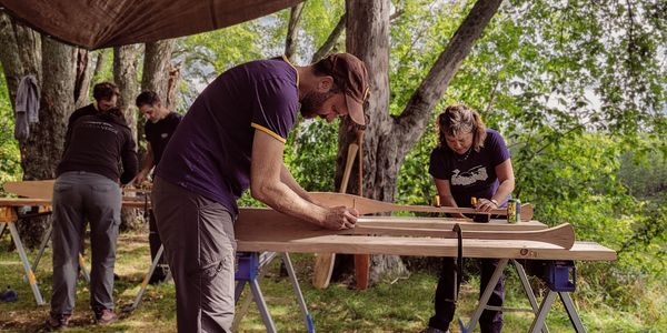 Students working on carving their canoe paddles outside