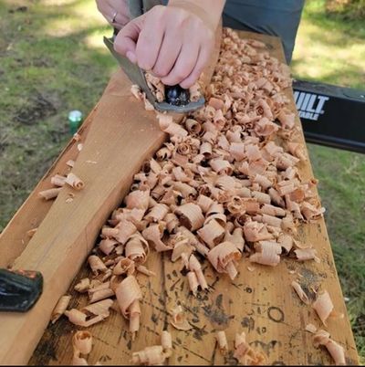 A zoom-in to a paddle being carved by a student with a woodworking plane.
