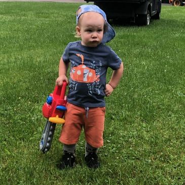 Toddler in blue shirt and orange shorts holding a toy chainsaw.