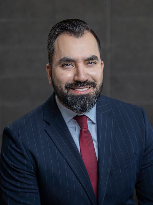 Man in a pinstripe suit with a red tie smiling.