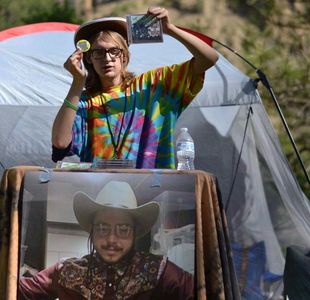 Person in tie-dye shirt holding items at outdoor booth.